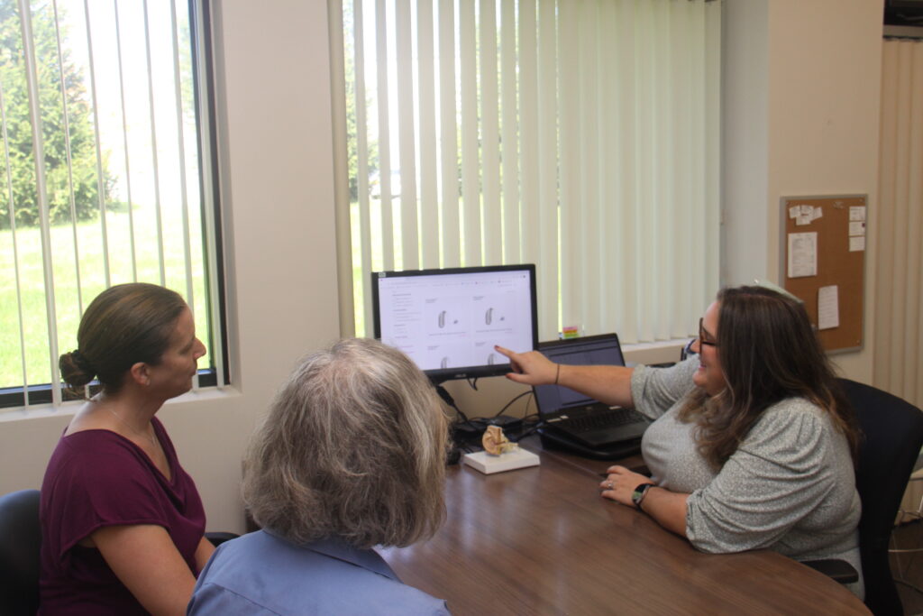 Woman showing two other women some hearing aid styles on a computer monitor